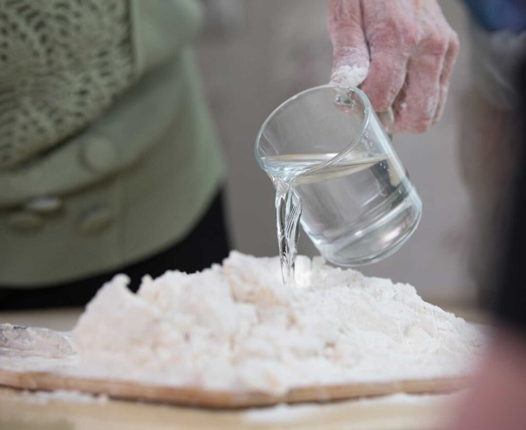 Acqua versata in una ciotola di farina per iniziare l’impasto.